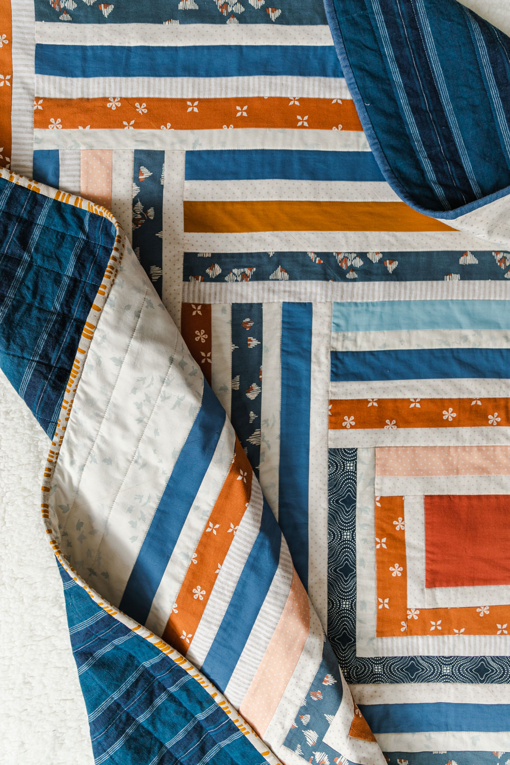 Sew a scrappy modern quilt with the Campfire quilt pattern. Based on the traditional log cabin quilt pattern, use long strips of fabric and scraps! suzyquilts.com #logcabinquilt #modernquilt