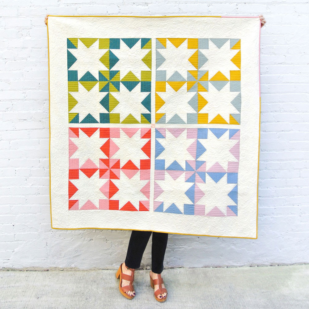 Easy Half Square Triangles Tutorial: A colorful Stars Hollow quilt held in front of a white wall. suzyquilts.com #quilting #sewingdiy