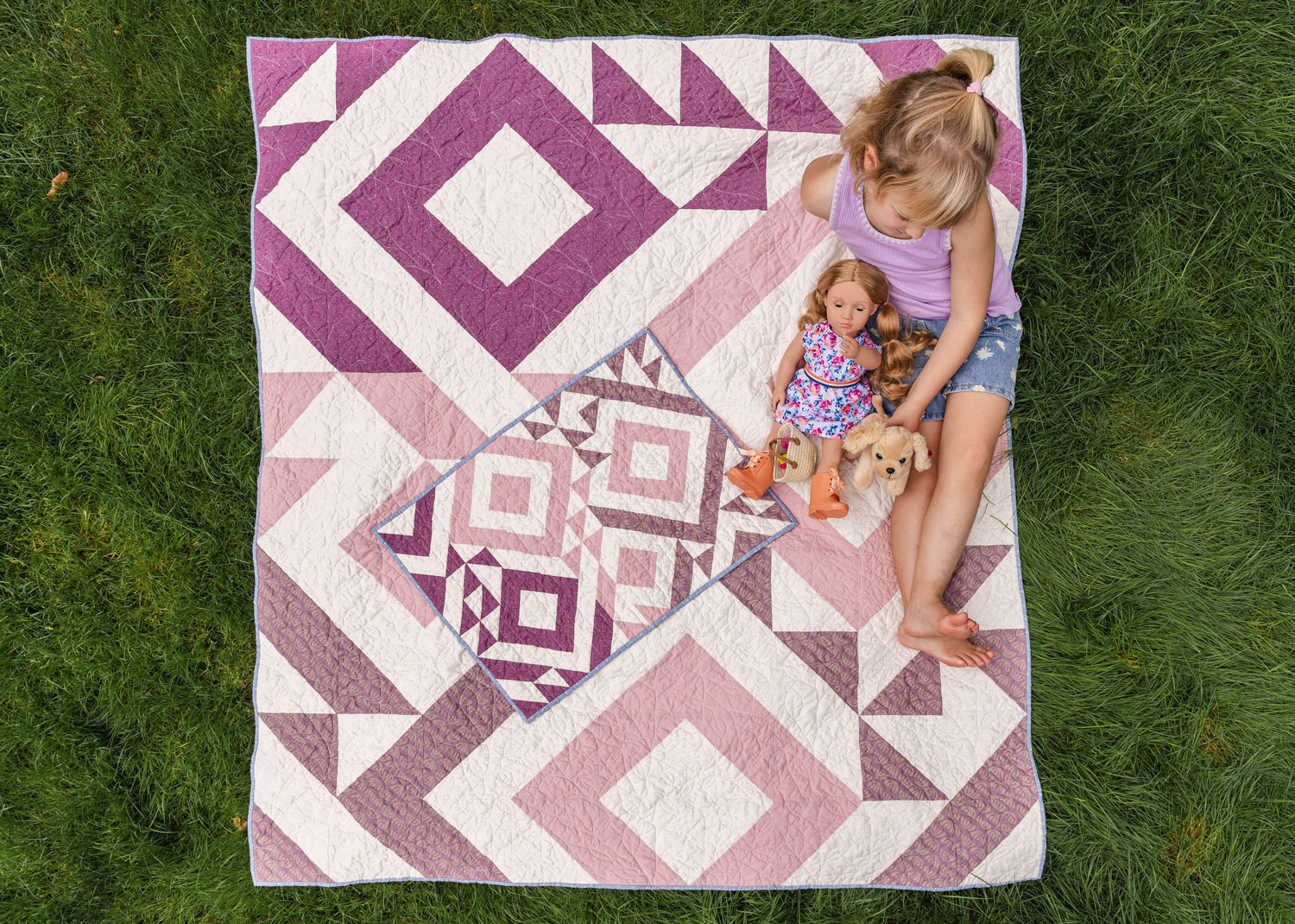 A little girl sitting on a Triangle Jitters quilt with her doll and matching doll quilt - suzyquilts.com A little girl sitting on a Triangle Jitters quilt with her doll and matching doll quilt - suzyquilts.com
